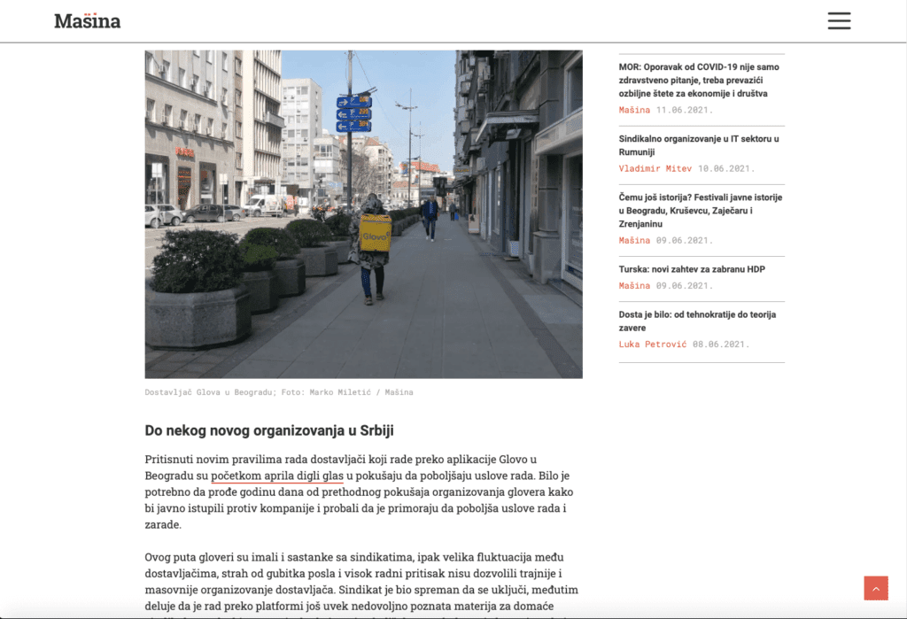 Особа која носи жути Glovo ранац за доставу хода широким градским тротоаром у Београду, окружена пешацима, паркираним аутомобилима и високим зградама – свакодневна сцена која пулсира контекстом и колективном солидарношћу.