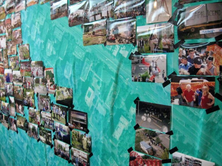Колаж разних фотографија је залепљен на зид боје тиркизне траке, приказујући сцене људи, активности на отвореном и догађаја. Неправилно распоређене фотографије одражавају колективну уметност и тренутке солидарности у свакодневном животу.